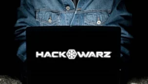 Person in a denim jacket using a laptop with the screen displaying "HACK WARZ" in bold white text.