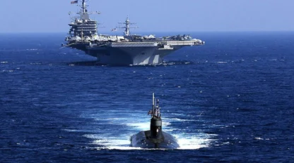 Submarine surfacing near an aircraft carrier on the ocean.