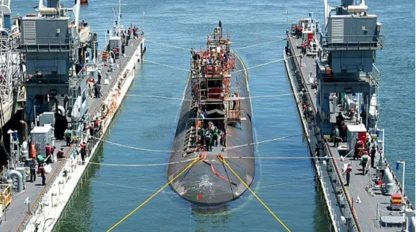 A submarine docked between two piers, with several people and equipment visible on the vessel and docks.