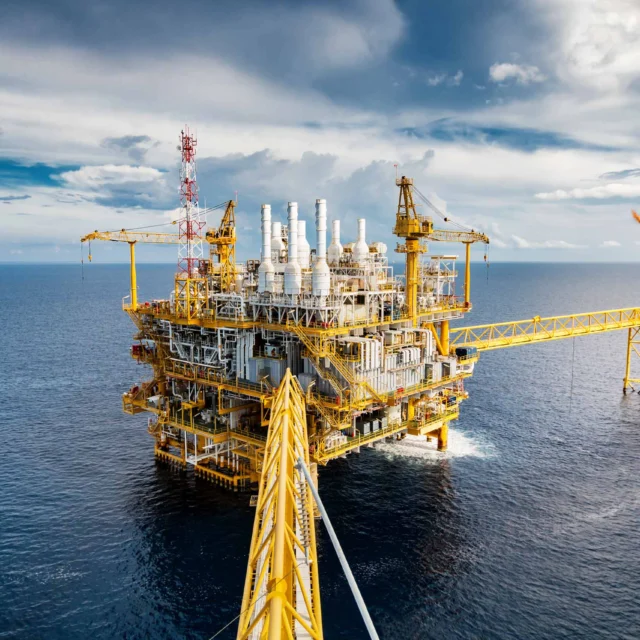 Offshore oil rig with three gas flares burning, surrounded by ocean under a cloudy sky.